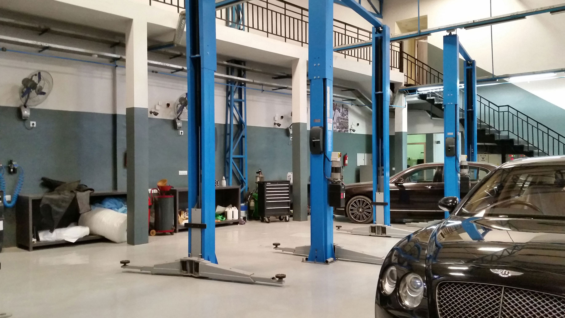 Two-storey workshop with two black cars  and some blue car lifts 