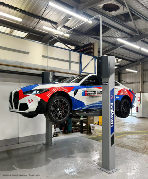 A white sports car with red and blue details is serviced in the workshop on a gray Ravaglioli 2-post lift