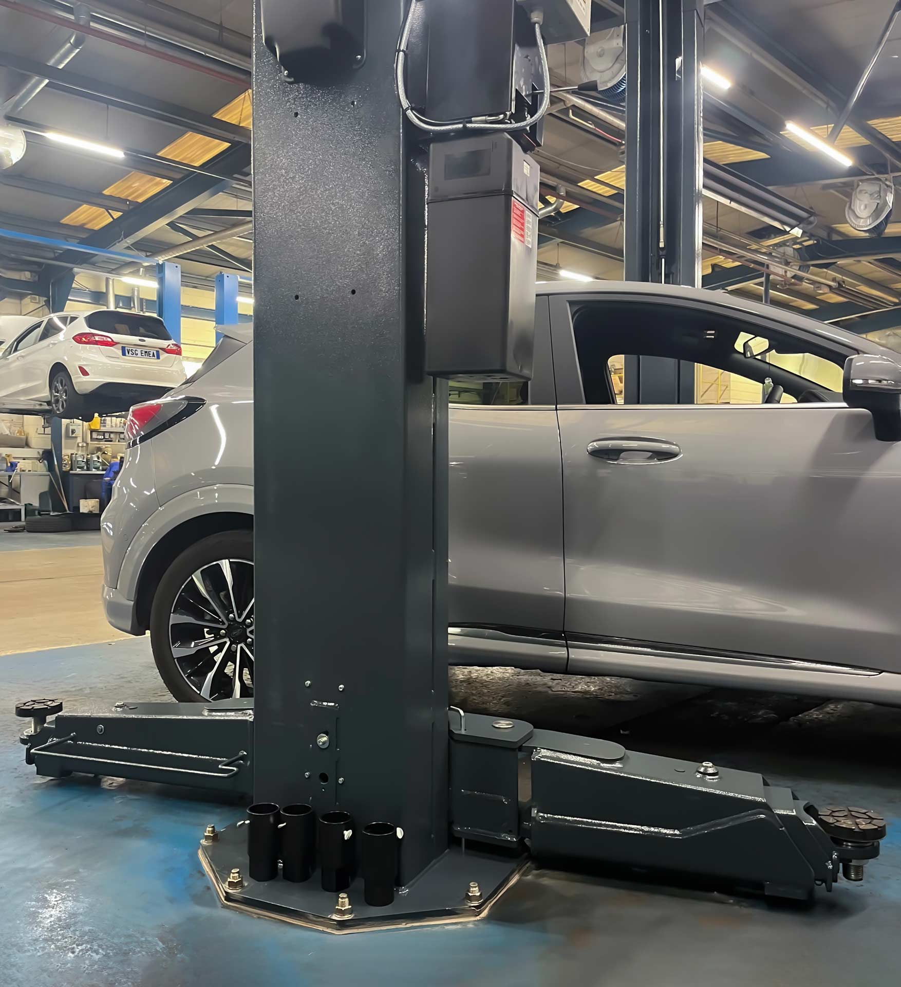 Dark gray column of a workshop car lift having two arms ready to lift a gray car