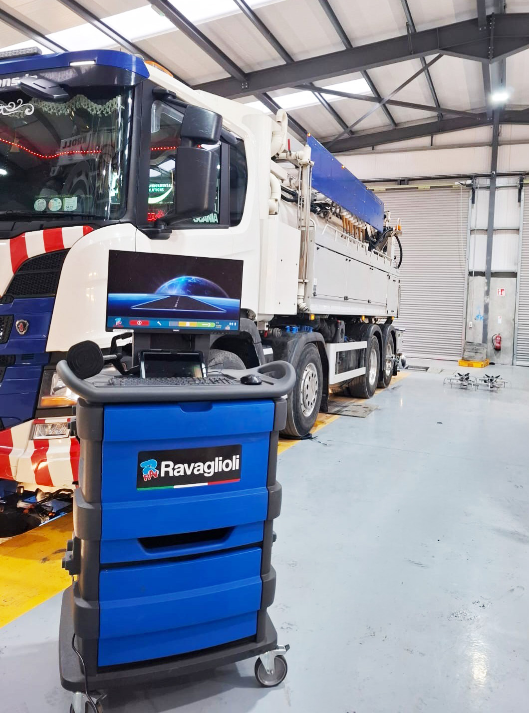 A blue Ravaglioli wheel aligner cabinet positioned in front of a white truck parked in a garage