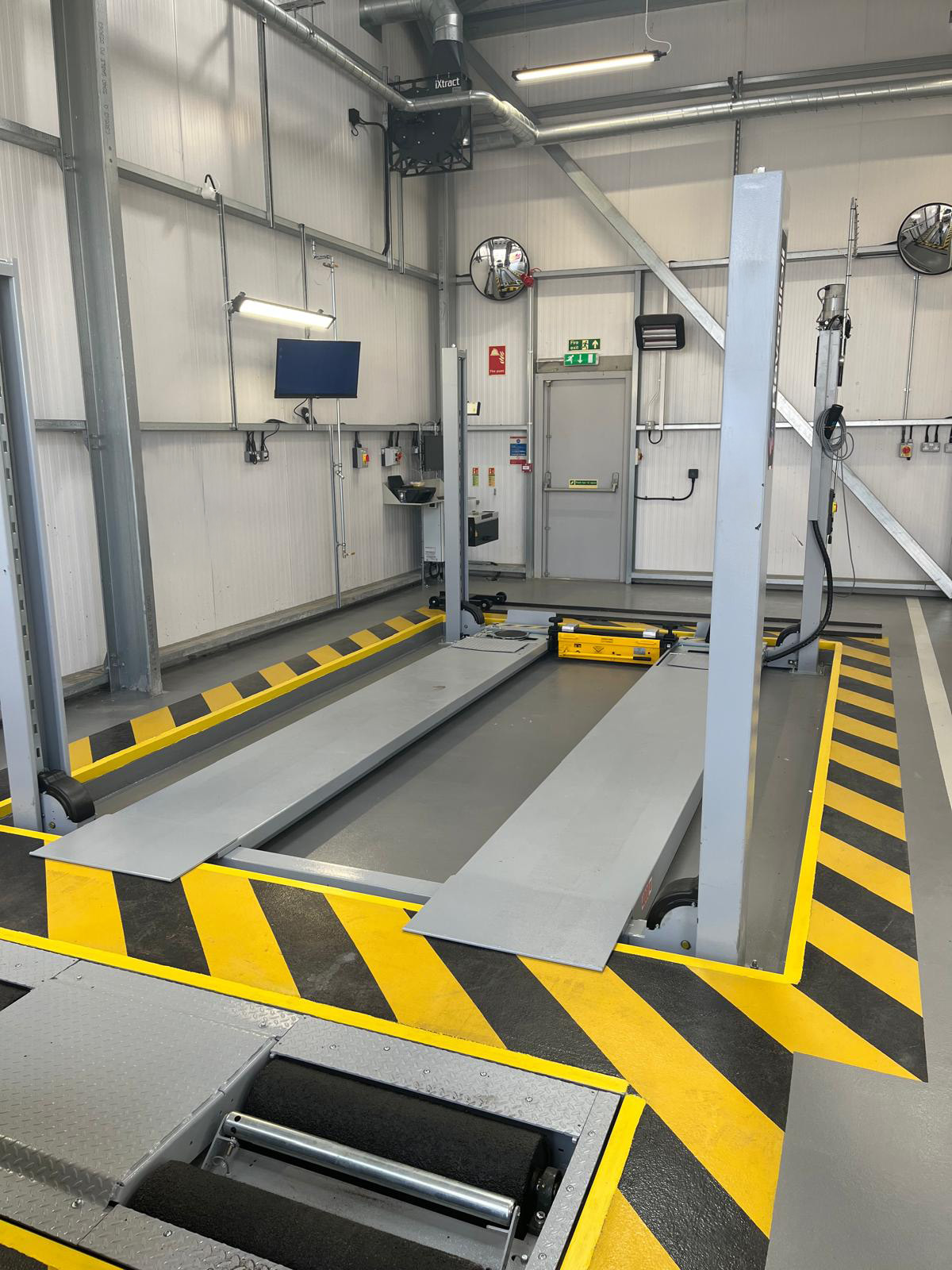 Gray 4-post lift installed in a workshop and bordered by yellow and black stripes