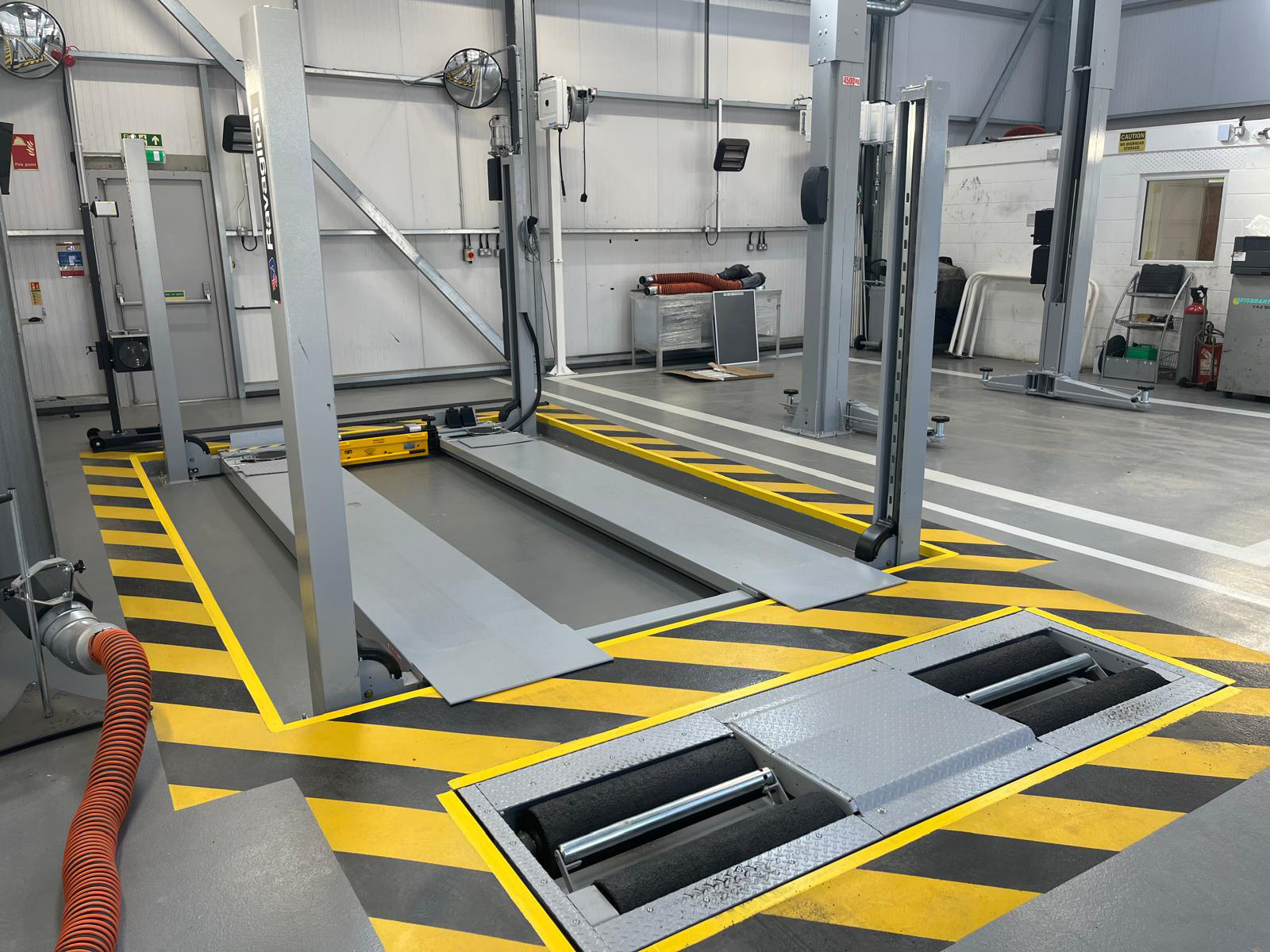 Gray 4-post lift and test lane installed in a garage and bordered by yellow and black stripes