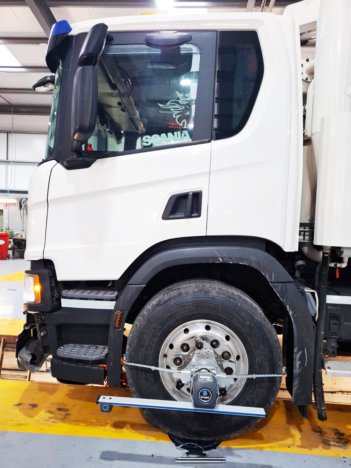 White Scania truck undergoing wheel alignment operation with a measuring head attached to the front wheel